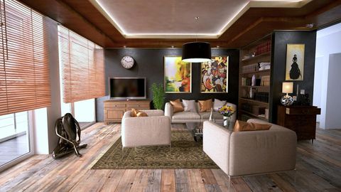A modern living room with beige sofas, wooden floors, large windows with blinds, a television, and dark-toned wall decor.