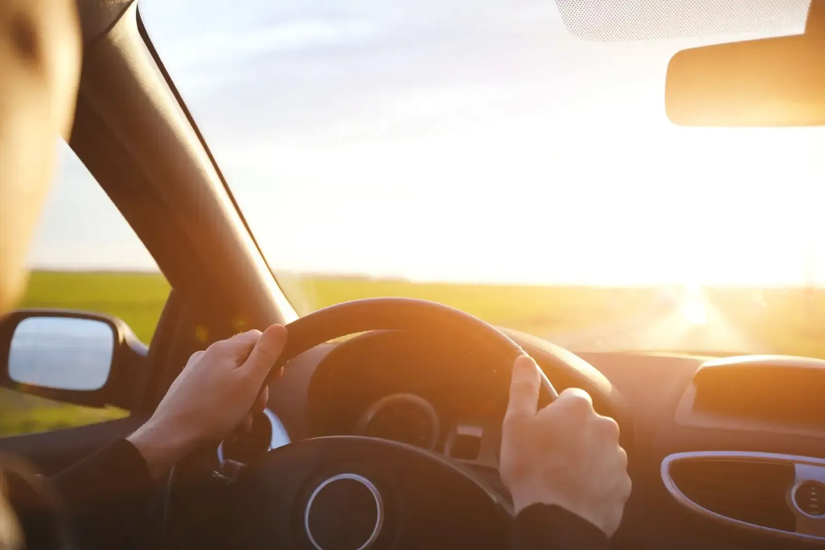 Una persona conduce un coche con el sol brillando a través del parabrisas.