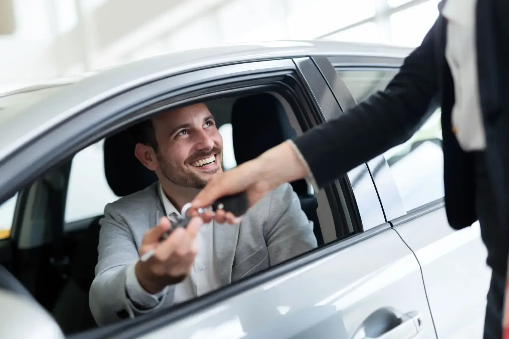 Un hombre está sentado en un coche mientras una mujer le da las llaves.