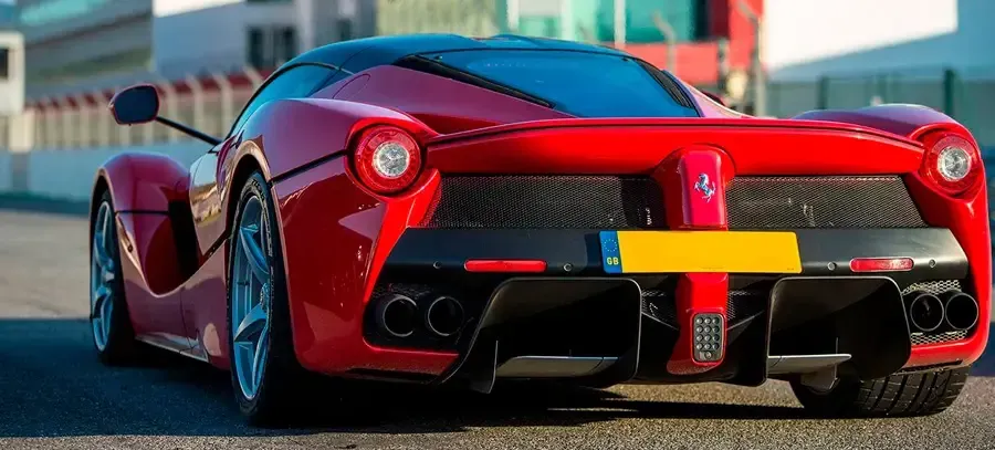 Un coche deportivo rojo con matrícula amarilla está estacionado al costado de la carretera.