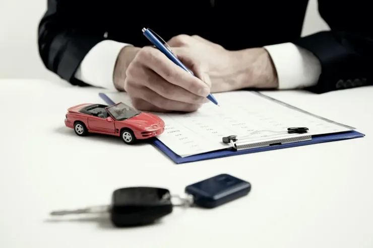 Un hombre está escribiendo en un portapapeles al lado de un coche de juguete y las llaves del coche.