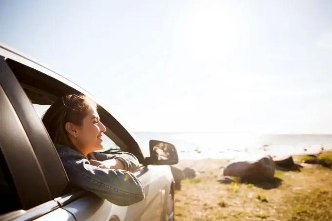 Una mujer está sentada en un coche mirando por la ventana hacia la playa.