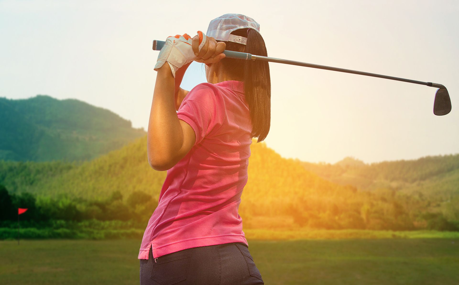 Pratique du golf par une jeune femme de dos.