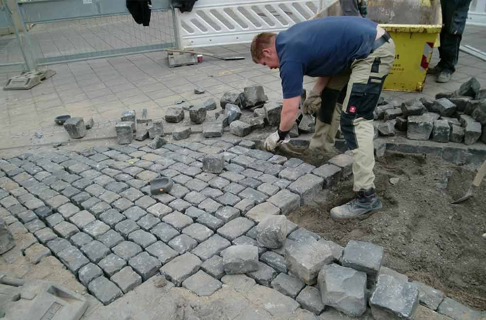 Ein Mann legt mit einer Schaufel Ziegel auf den Boden