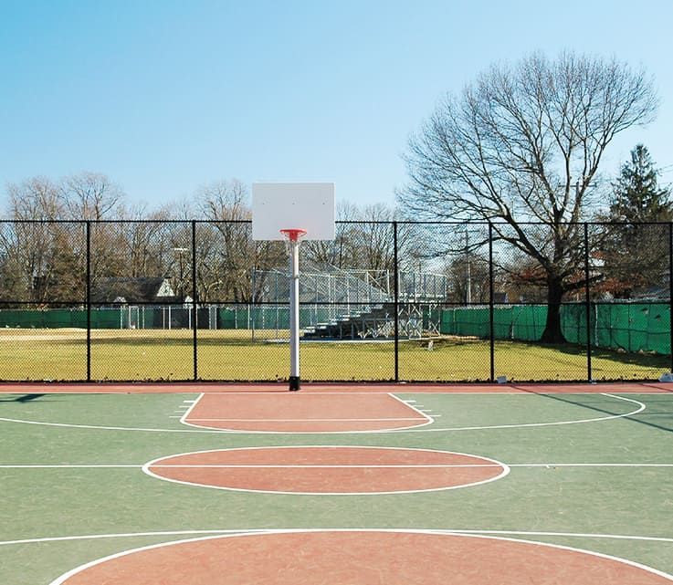Ein leerer Basketballplatz mit einem Zaun und Bäumen im Hintergrund