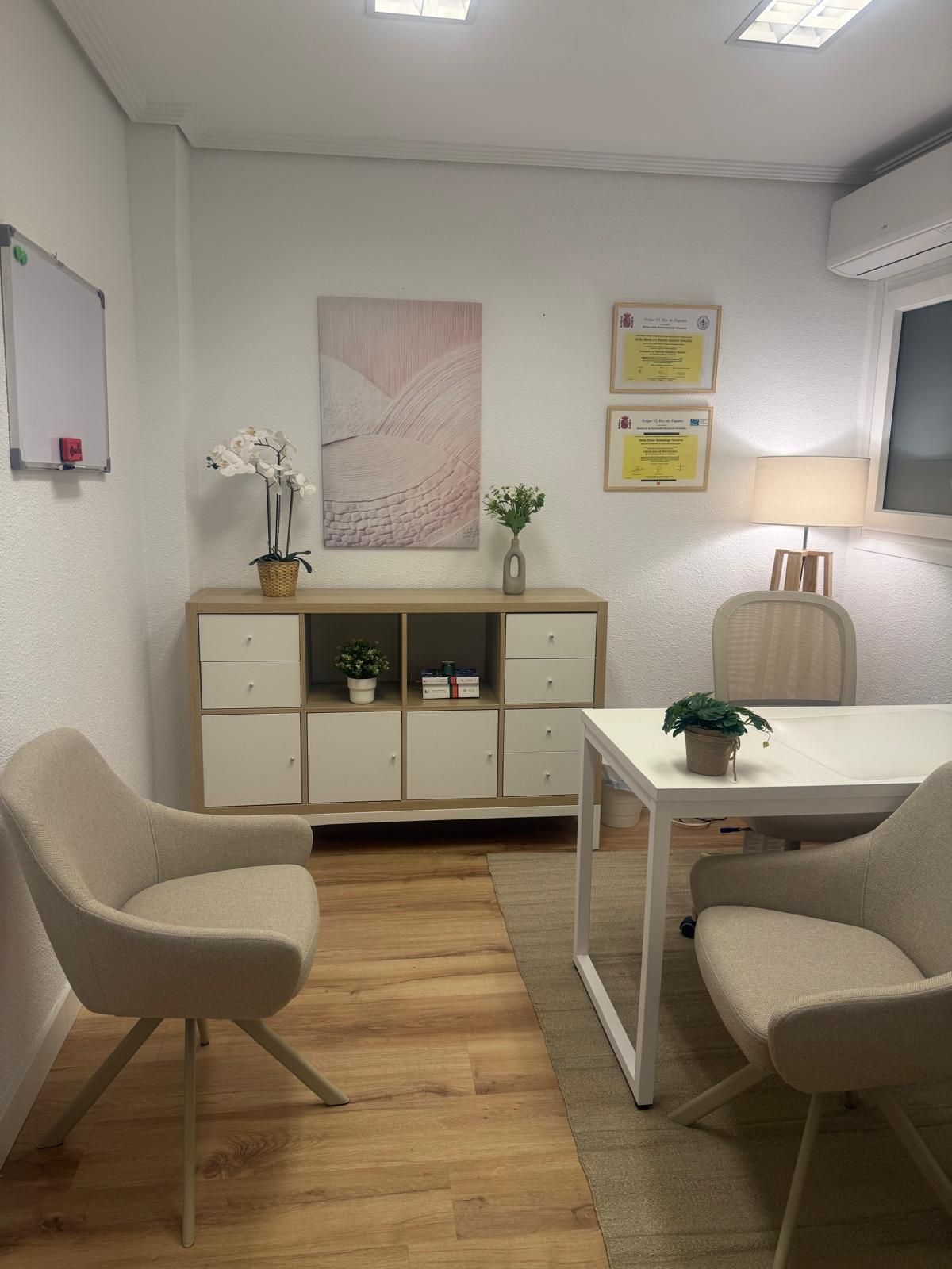 Acogedora sala de espera de oficina con sillas beige, mesa blanca, armario, cuadros en la pared