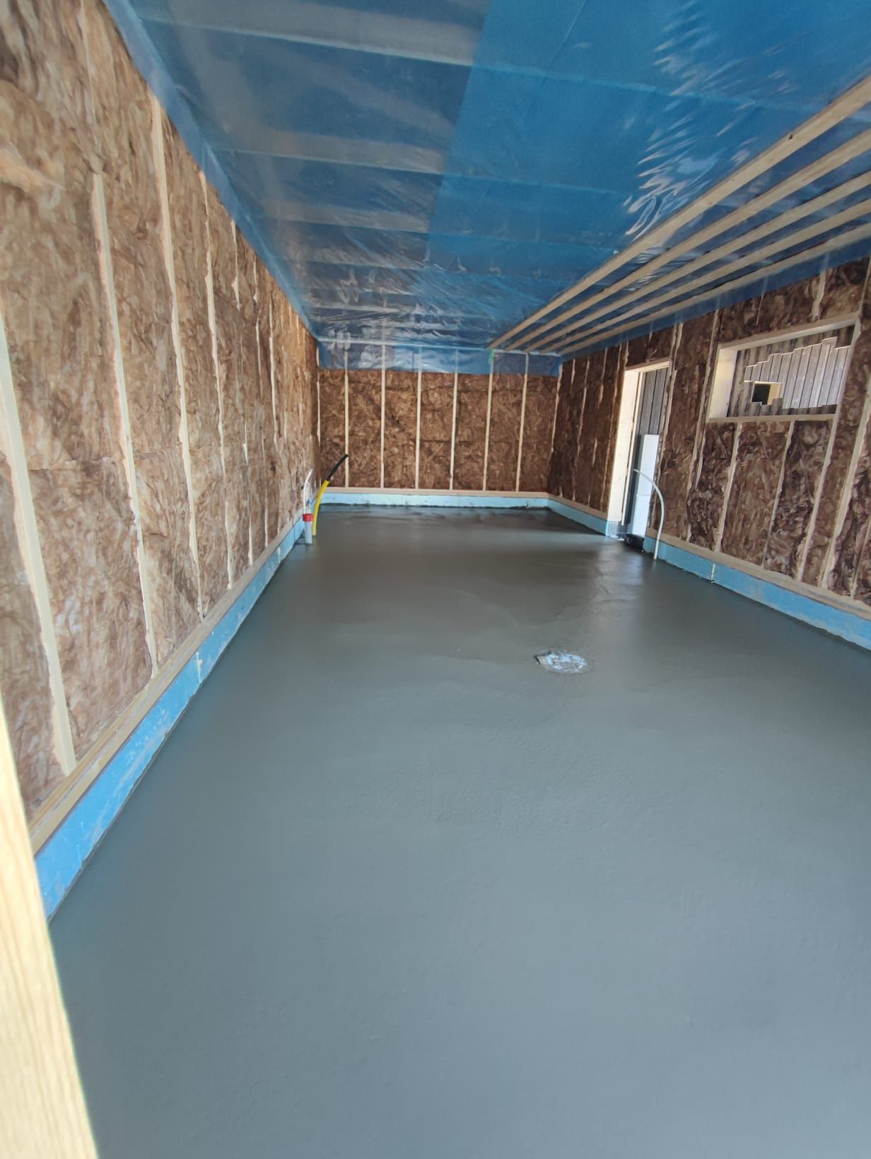 Huoneen sisätilat, joissa on harmaa betonilattia, eristetyt seinät ja sininen katto; rakenteilla.