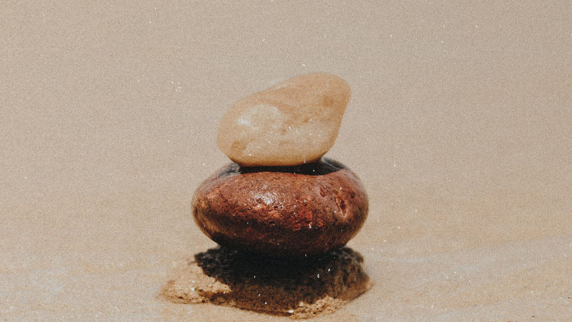Two stacked stones on a sandy beach, with a small pebble balanced on top