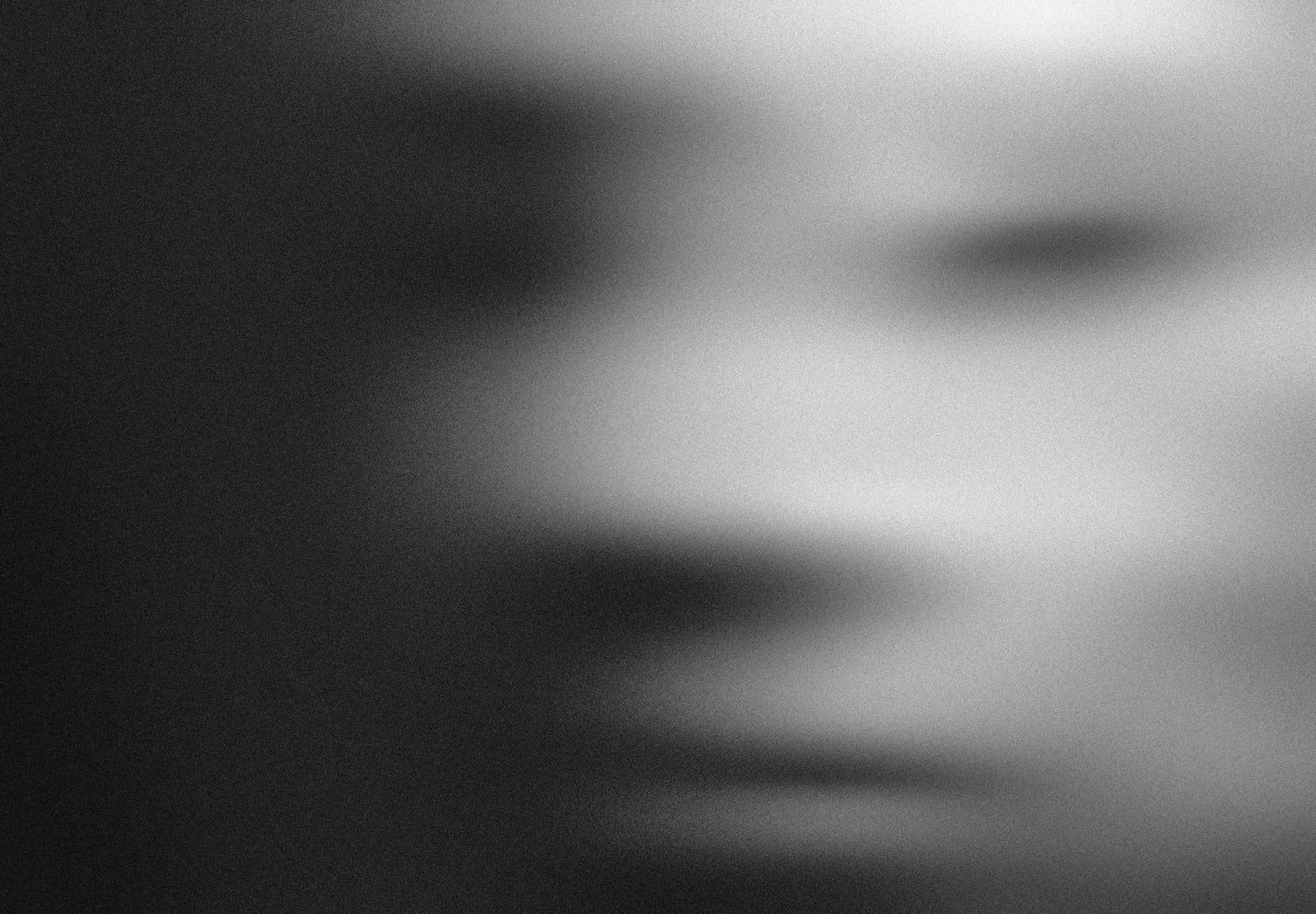 Blurred grayscale close-up of a human face, showing one eye, nose, and mouth in soft focus