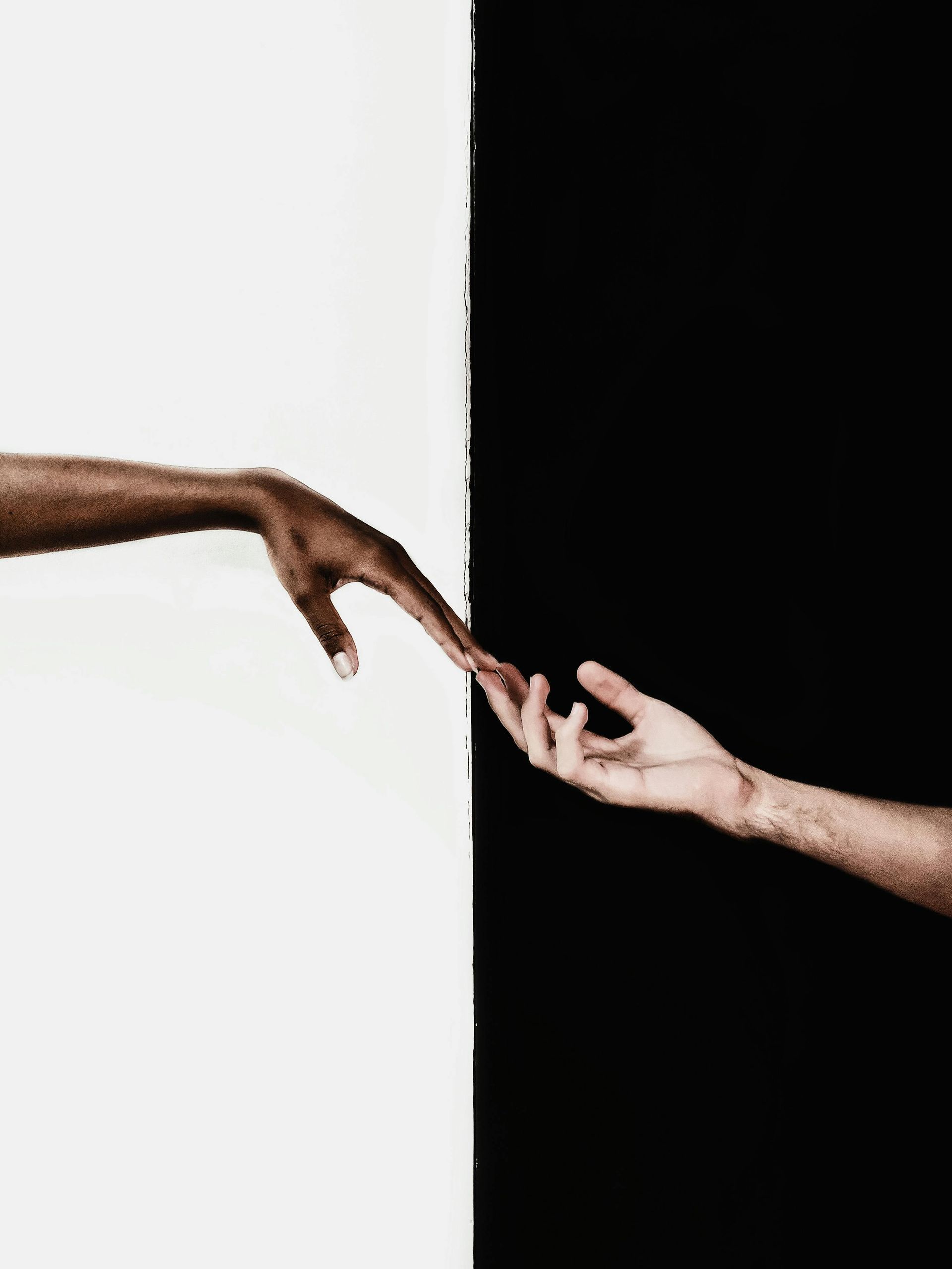 Two hands reaching toward each other against a split background, half white and half black.
