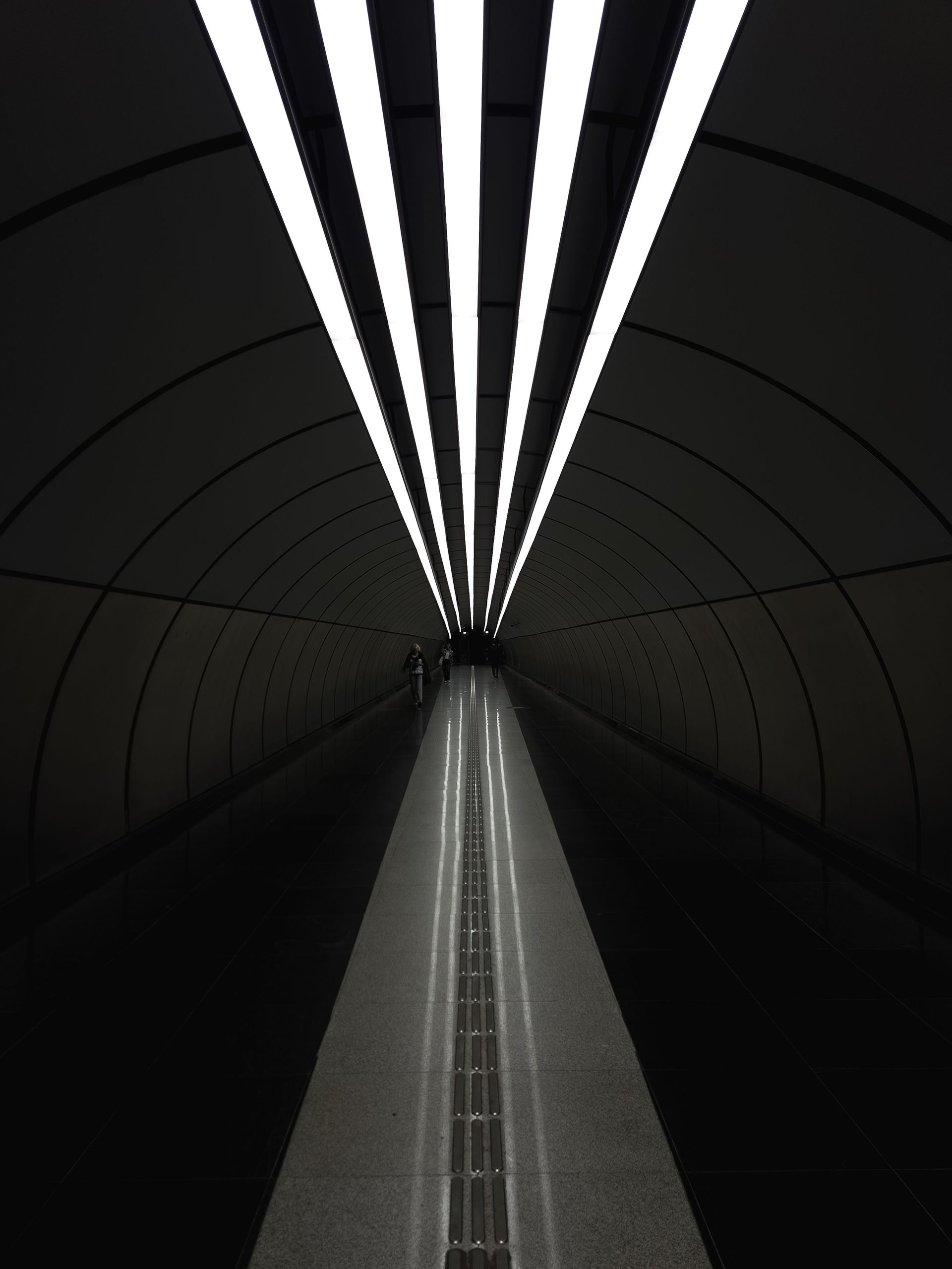 Futuristic tunnel with bright white ceiling lights and a reflective central walkway.
