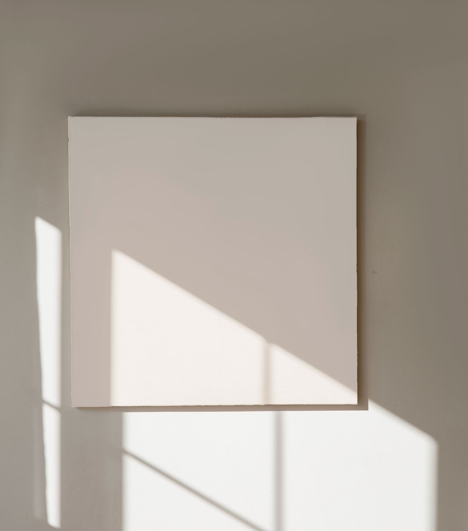Minimalistisches Interieur mit einer leeren Leinwand, sanften Sonnenschatten und einer kleinen Keramikvase auf weißem Grund