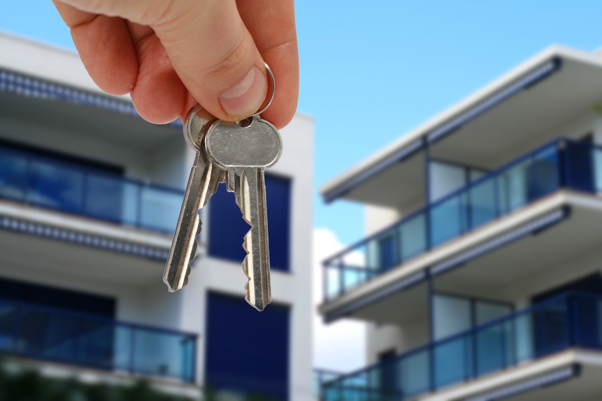 Un main tenant des clefs devant des immeubles.
