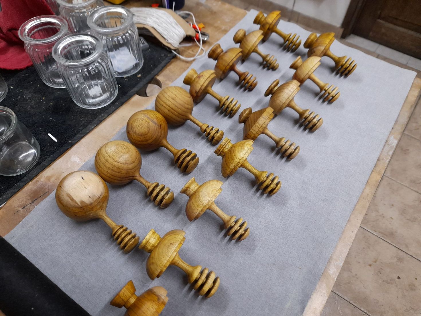 Cucharas de madera para miel sobre una superficie gris con tarros de cristal al fondo.