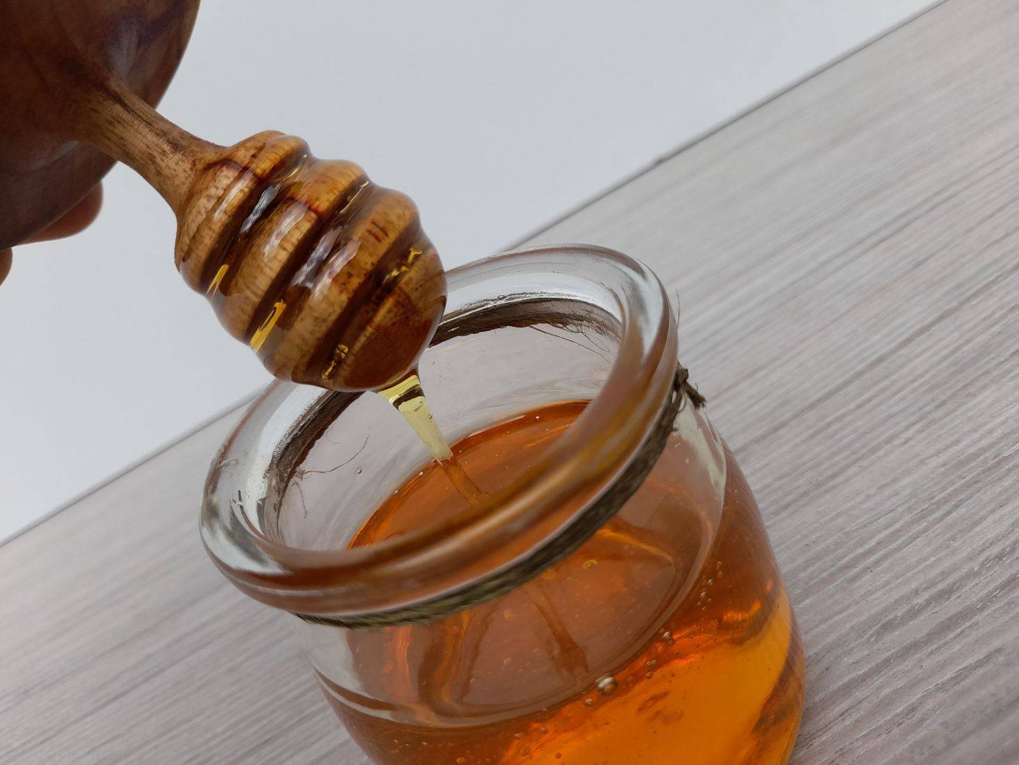 Miel goteando de un cucharón de madera a un pequeño tarro de cristal lleno de miel.