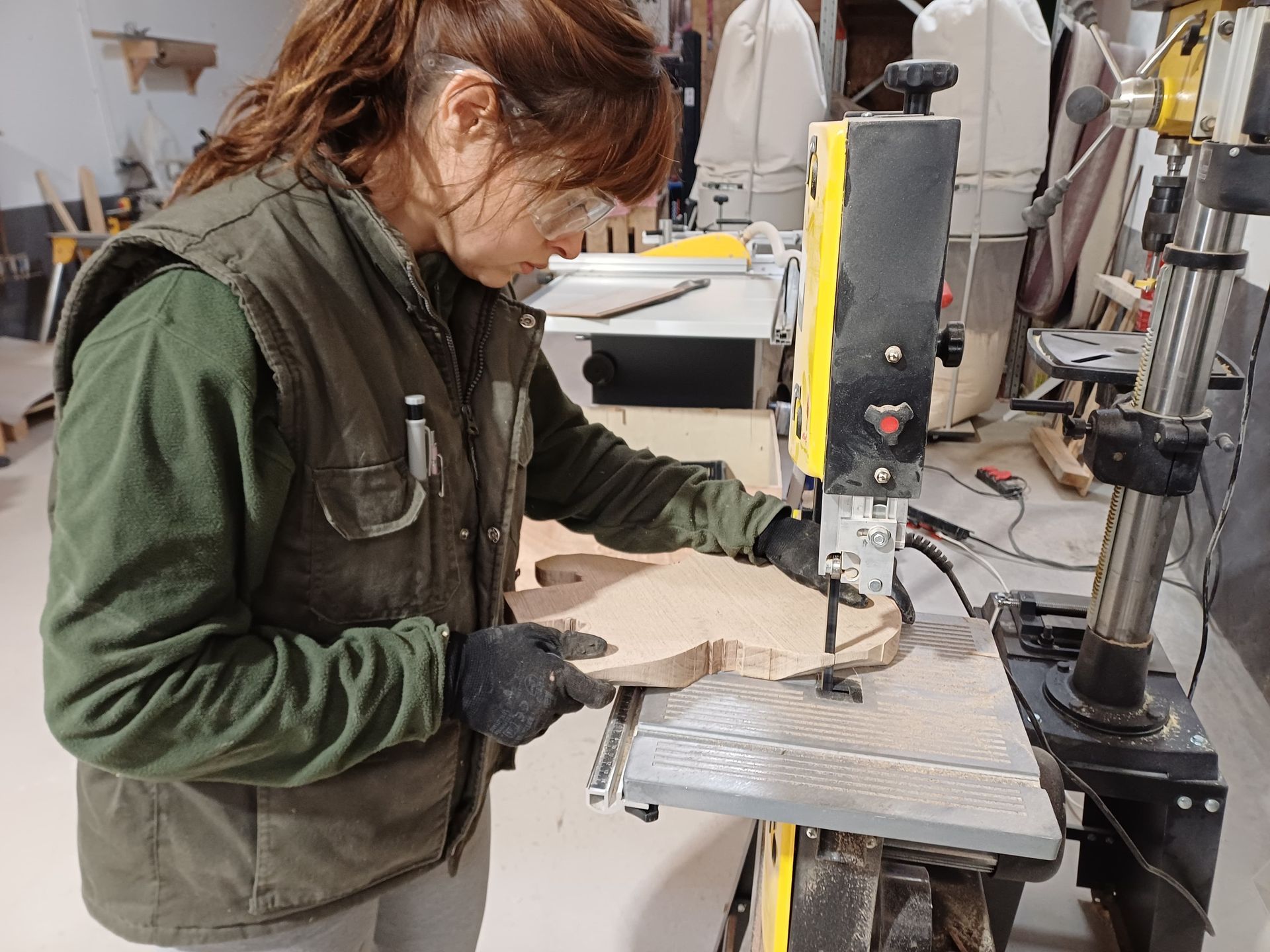 Mujer utilizando una sierra de cinta, con gafas y guantes de seguridad, en un taller.