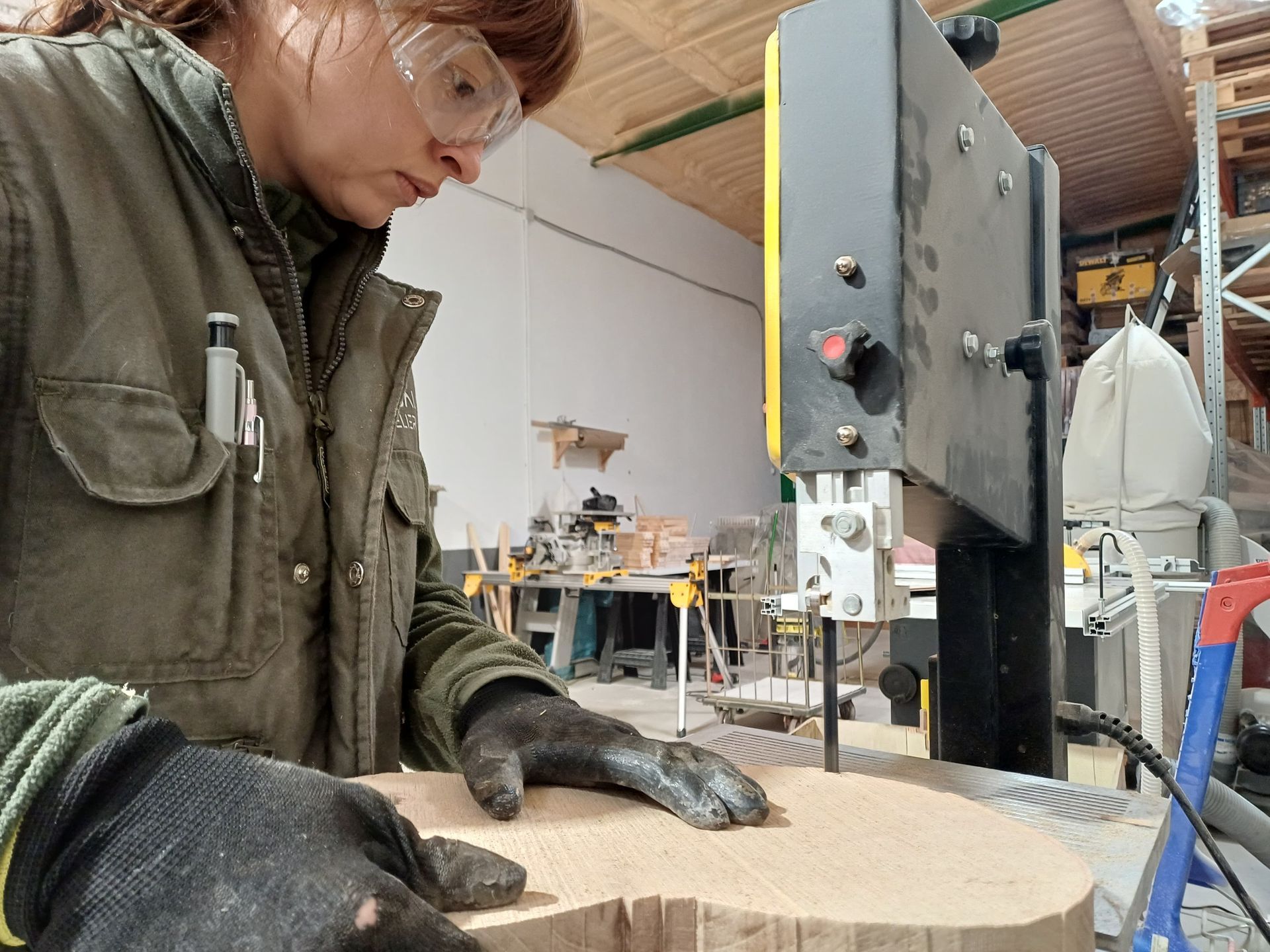 Una mujer con gafas de seguridad corta madera con una sierra de cinta en un taller.