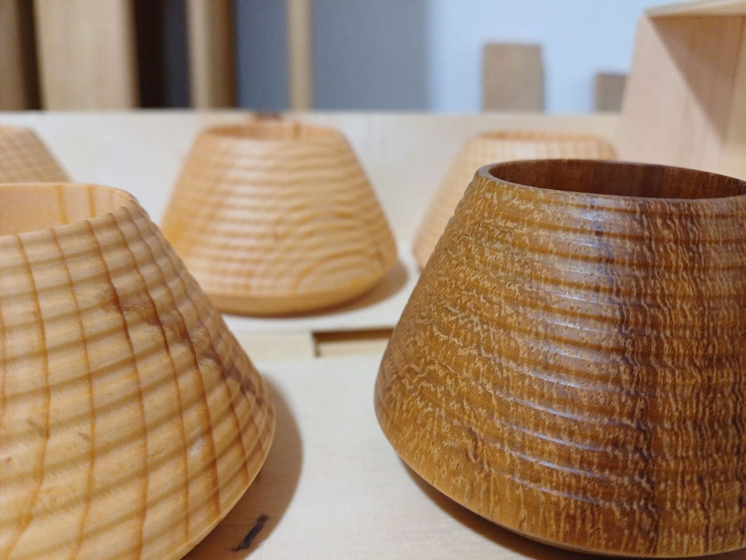 Tazas de madera tallada con diversos diseños y colores, colocadas sobre una superficie de madera clara.