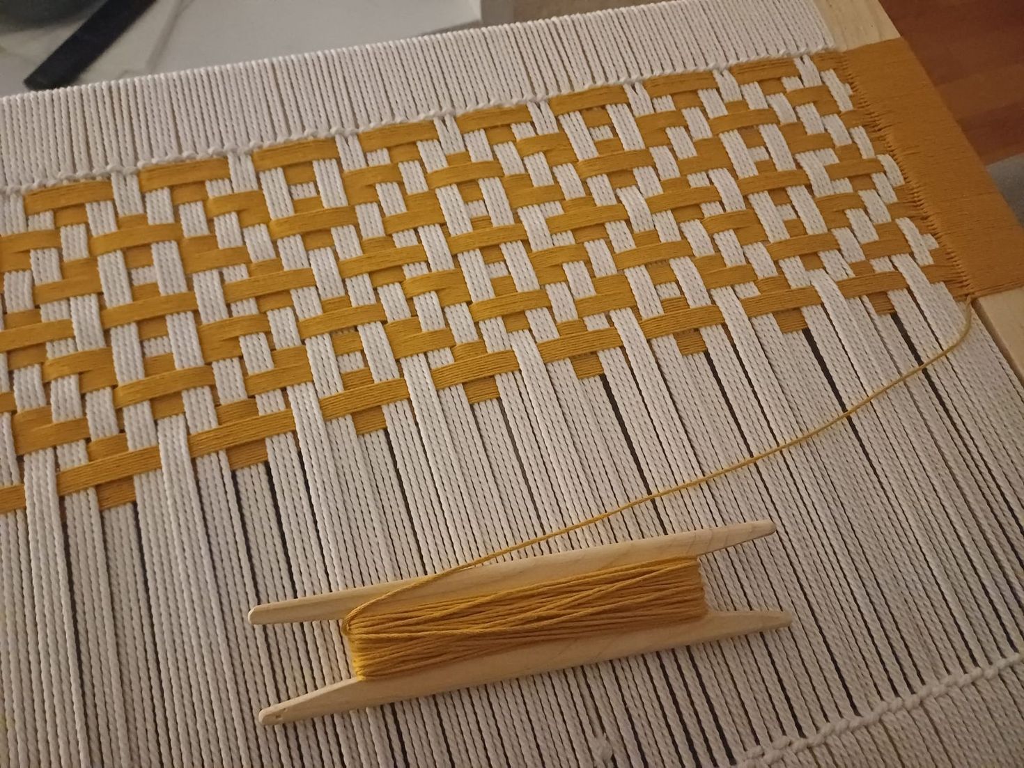 Proyecto de tejido en progreso. Hilos amarillos y blancos entretejidos en un telar.
