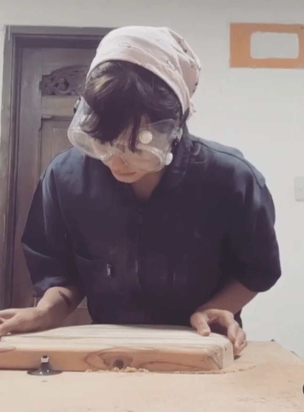 Persona que lleva protección ocular y gorro, trabajando con madera.