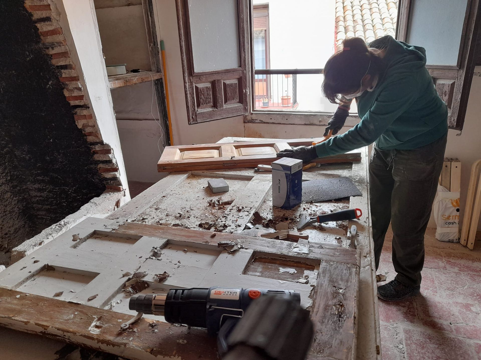 Persona trabajando en una puerta en una habitación, utilizando herramientas. La habitación tiene una ventana y ladrillo visto