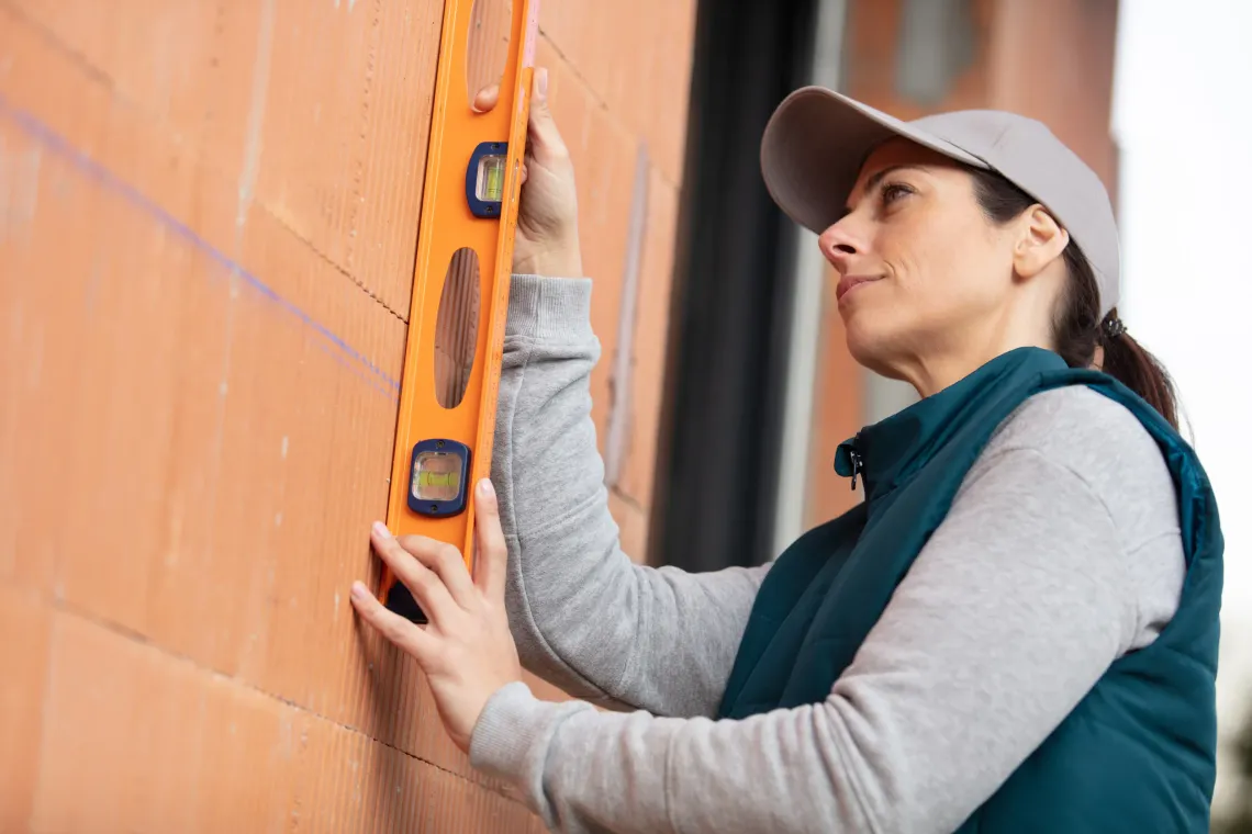 Mujer usando un nivel en una pared de ladrillos naranja, al aire libre.