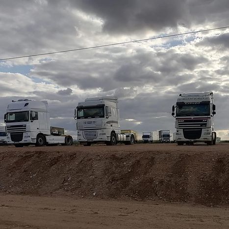 Tres camiones semirremolque están estacionados en un campo de tierra en un día nublado.