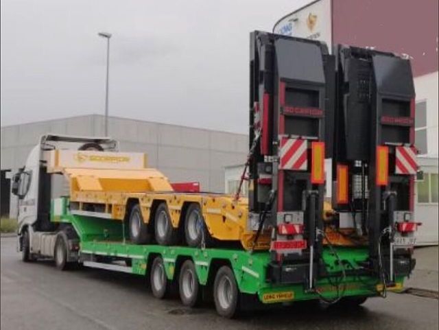 Un camión semirremolque verde y amarillo está estacionado frente a un edificio.
