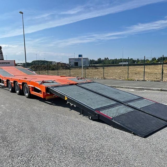 Un remolque de plataforma con rampas está estacionado al costado de la carretera.