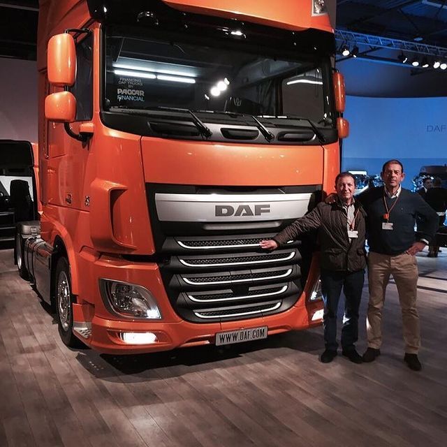 Dos hombres posan frente a un camión DAF naranja