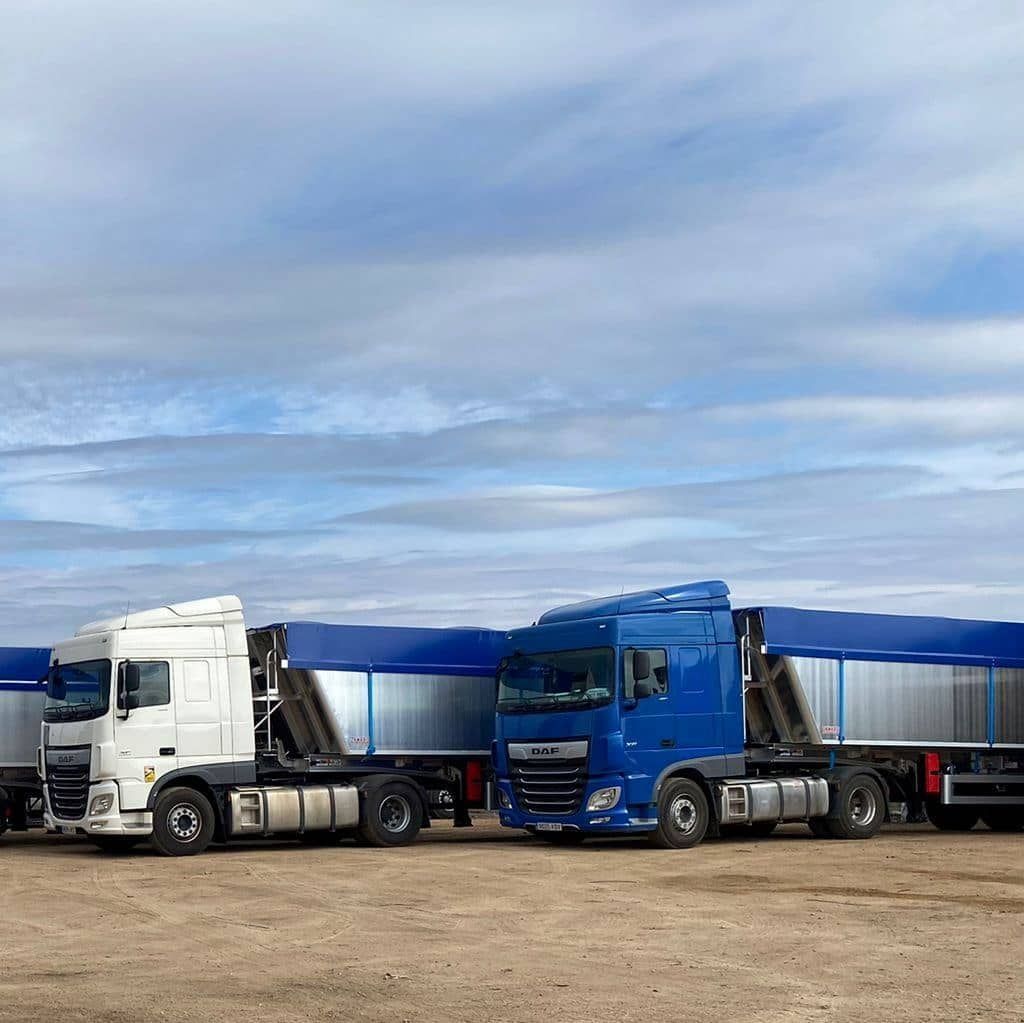 Dos camiones están estacionados uno al lado del otro en un campo de tierra.