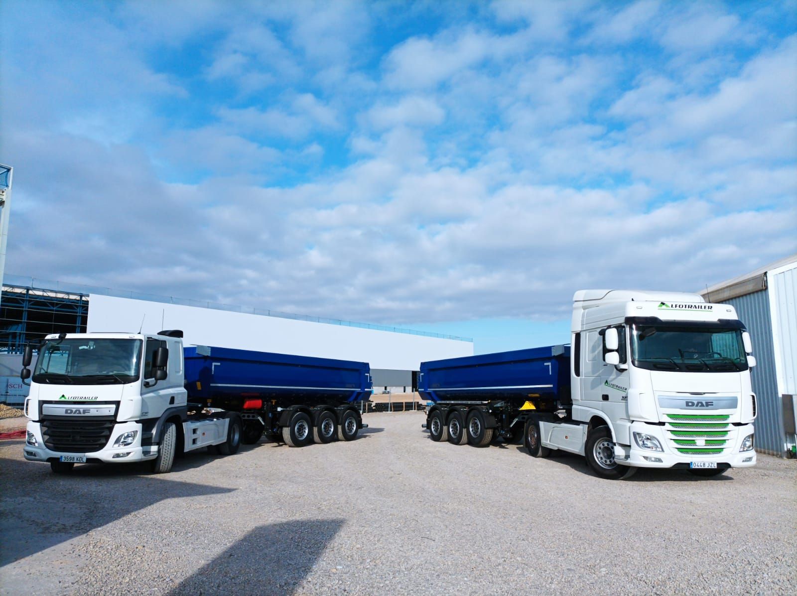 Dos camiones semirremolque están estacionados uno al lado del otro en un estacionamiento de grava.