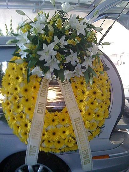 Una corona de flores amarillas y blancas reposa en la parte trasera de un automóvil plateado.