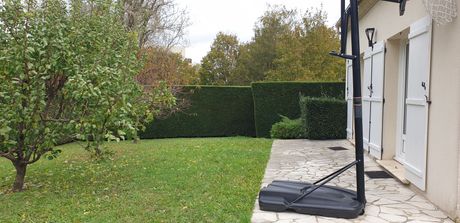 Jardin avec pelouse verte, haies, arbres et terrasse de maison à côté d'un panier de basket.