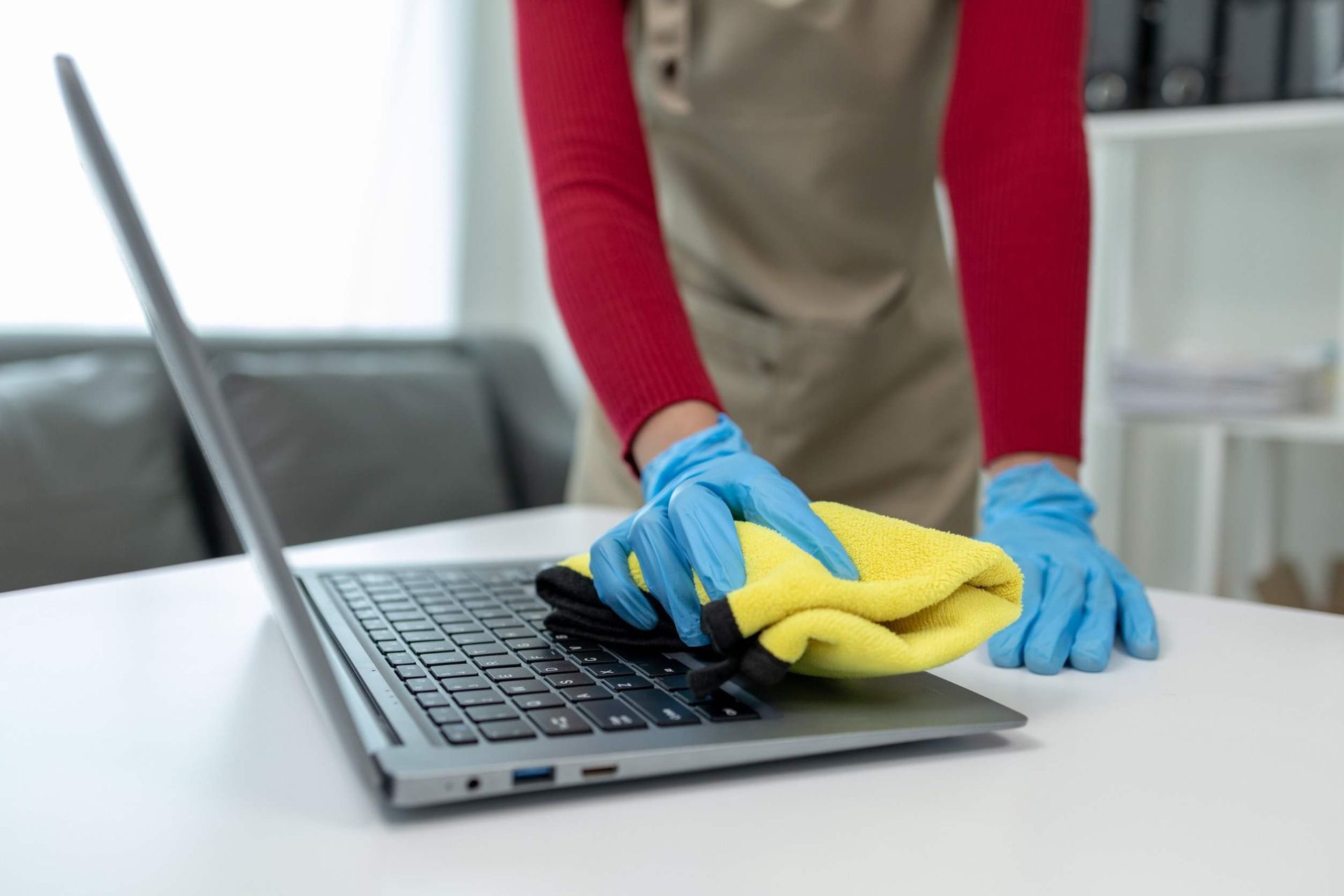 Una persona está limpiando una computadora portátil con un paño y guantes.
