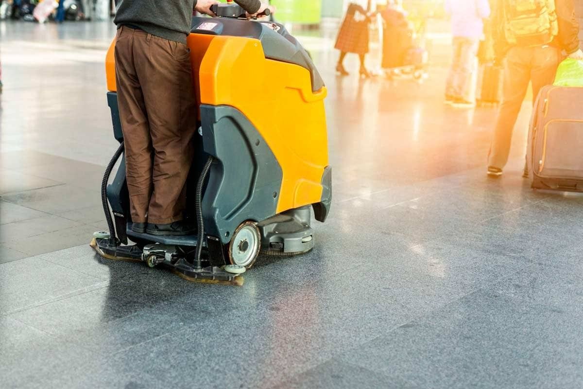 Un hombre está limpiando el suelo de un aeropuerto con una máquina.