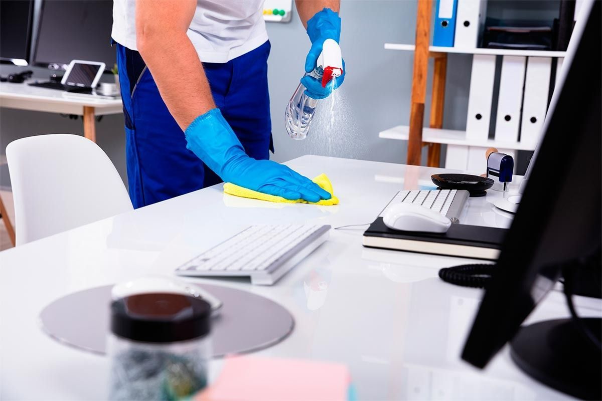 Un hombre está limpiando un escritorio en una oficina con una botella de spray.