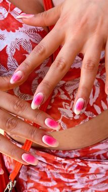 Manos con uñas ombré rosas y blancas, apoyadas sobre tela estampada roja y blanca.
