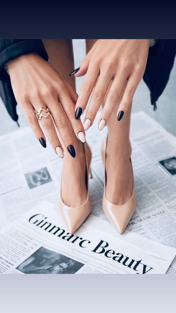 Manos con esmalte de uñas negro y nude, apoyadas sobre un periódico con tacones altos en primer plano.