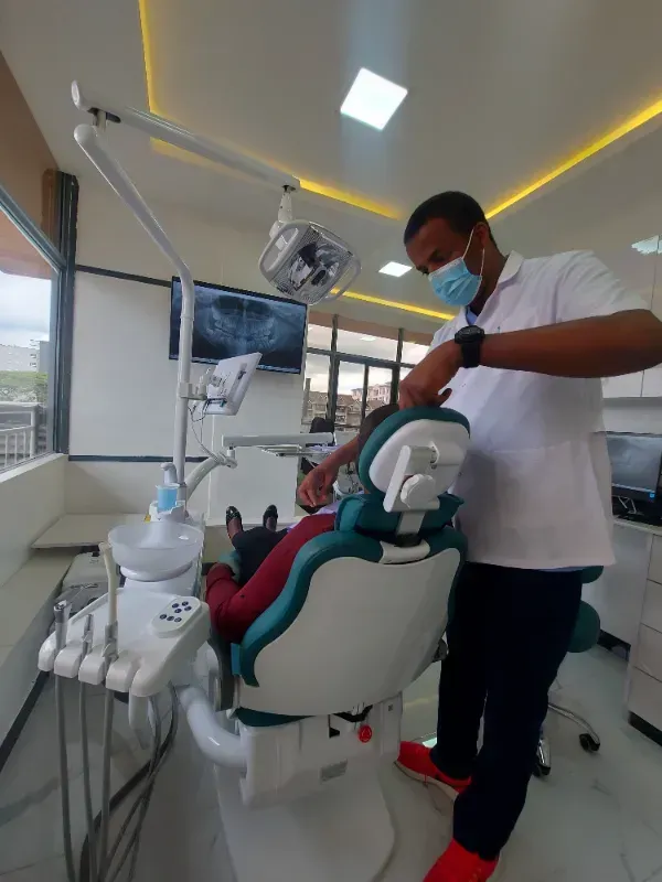 Dentist treating a patient in a modern clinic, with overhead light and dental chair equipment.