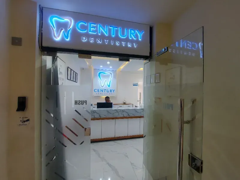 Century Dentistry reception desk with blue neon tooth sign in a modern white office entryway