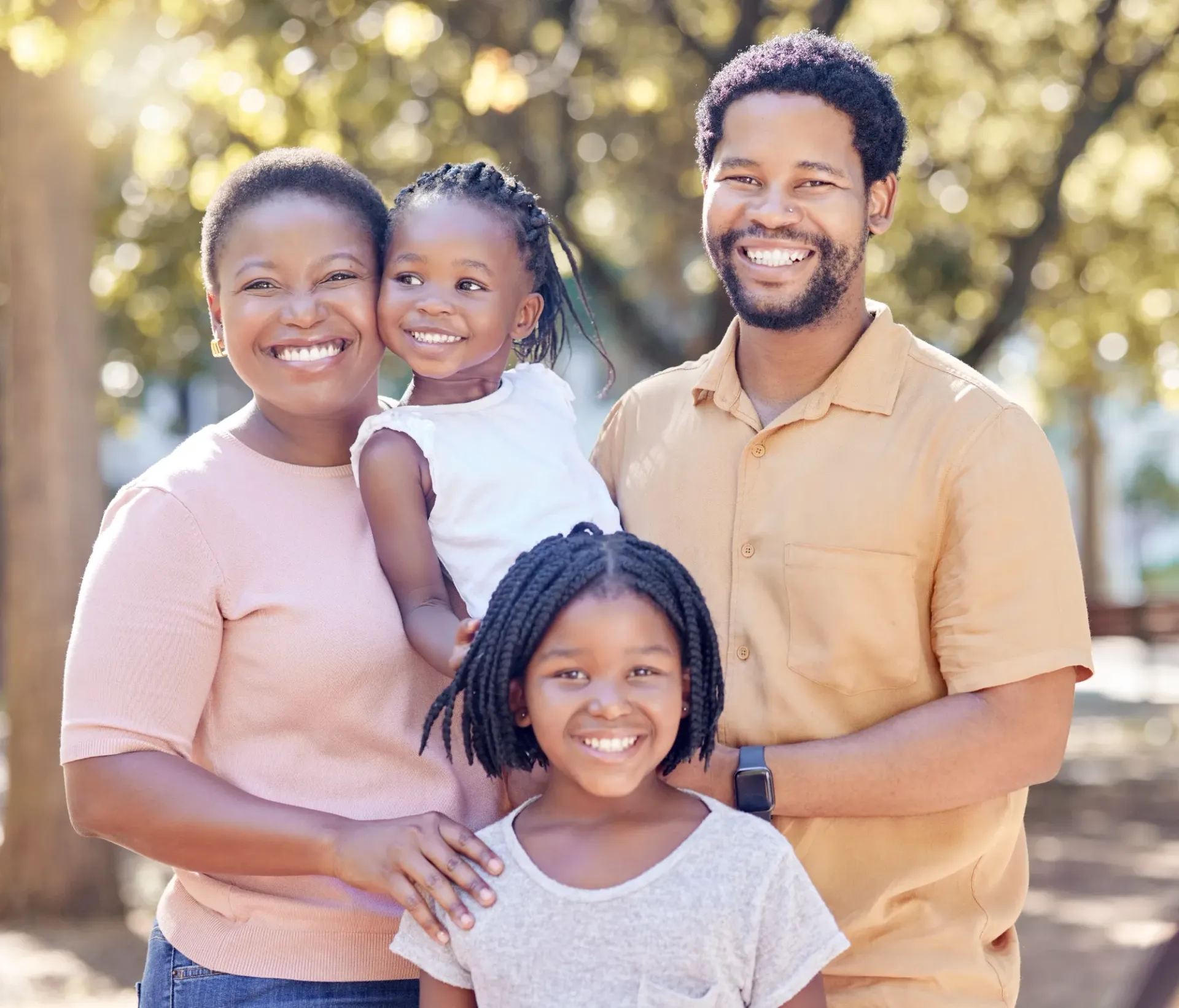 Smiling family of four standing outdoors in soft sunlight