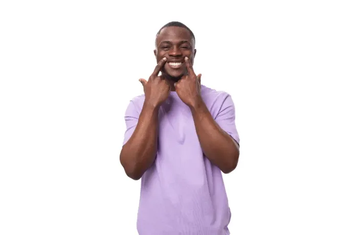 Smiling man in a purple shirt, touching his cheeks with both hands against a white background