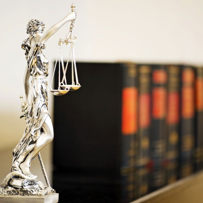 Statue de la Justice en argent devant des livres de droit flous sur une étagère
