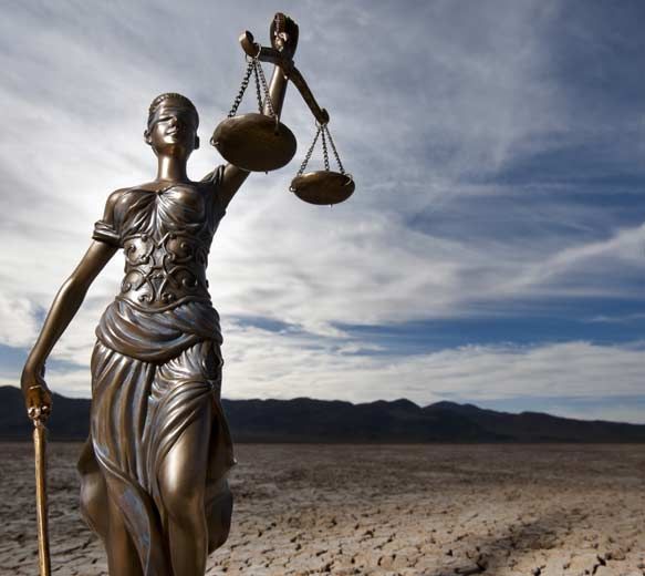 Statue en bronze de la Dame Justice tenant une balance dans un désert aride sous un ciel nuageux