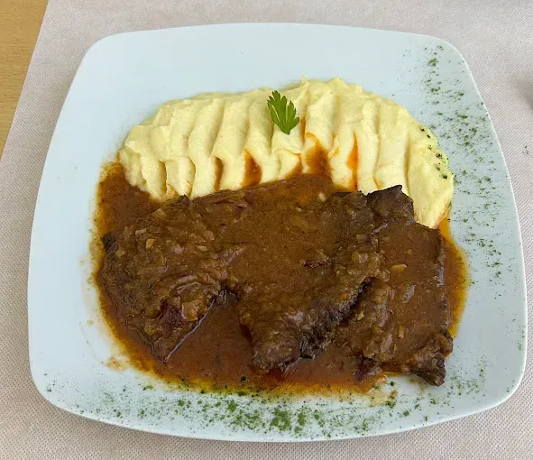 Un plato blanco cubierto con carne y puré de papas.