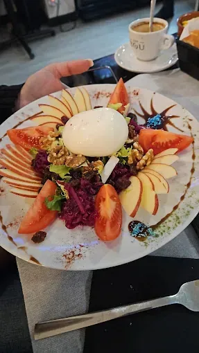 Una persona sostiene un plato de comida con una taza de café en el fondo.
