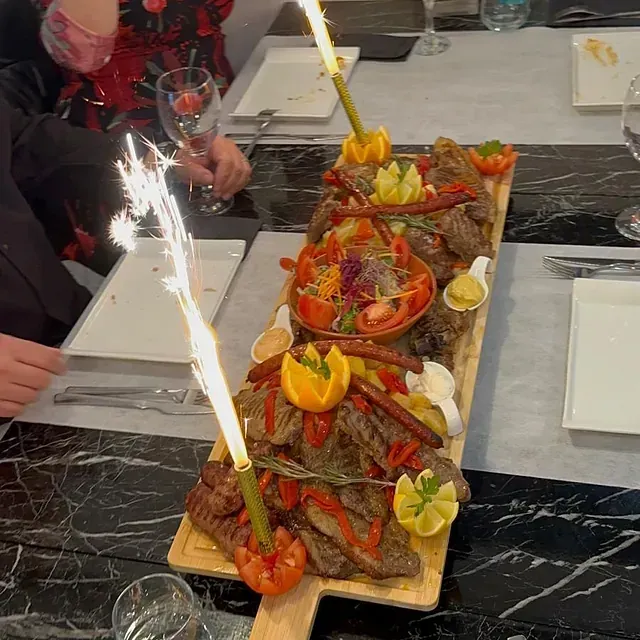 Una larga tabla de cortar de madera llena de comida y bengalas sobre una mesa.