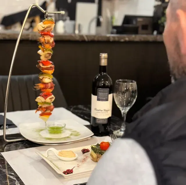 Un hombre se sienta a una mesa con una botella de vino y platos de comida.
