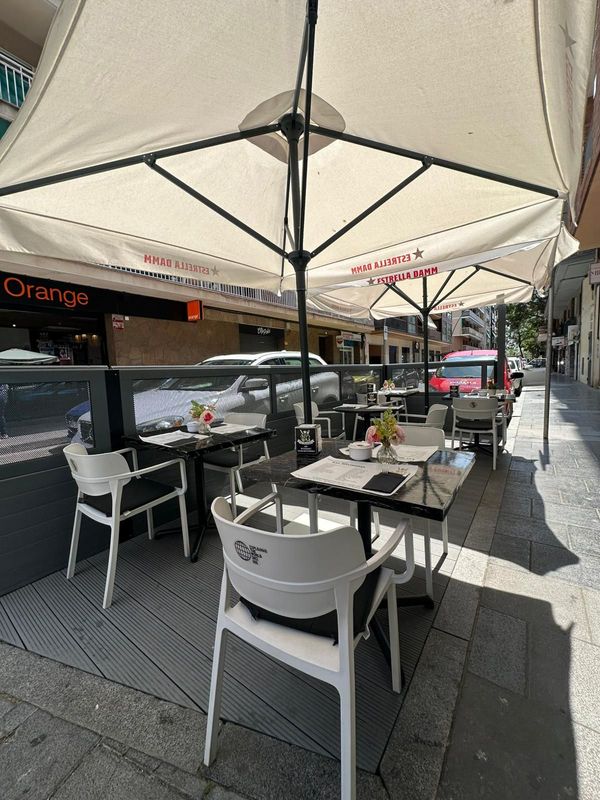 Un cartel de restaurante está en la acera al lado de una acera con mesas y sillas.